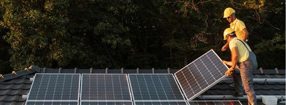 Dos técnicos instalando paneles solares en el techo de una vivienda al atardecer